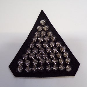 May include: A black triangular patch covered in silver pyramid-shaped studs.