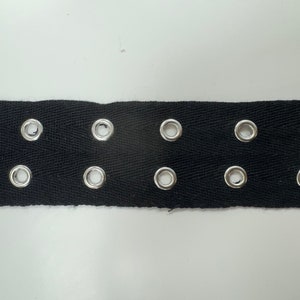 May include: Black webbing with silver metal eyelets. The webbing has a herringbone pattern.