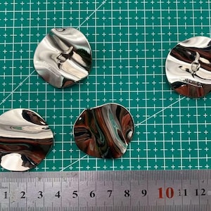 May include: Four silver-coloured metal buttons with a wavy, textured surface. The buttons are circular and have a small hole in the centre.