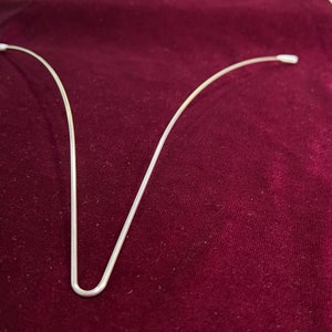 May include: Three silver wire hair hoops, bent into a U shape, on a dark red velvet surface.