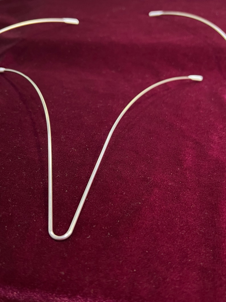 May include: Three silver wire hair hoops, bent into a U shape, on a dark red velvet surface.