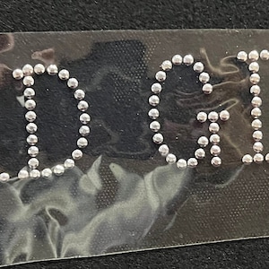 Op de afbeelding: Een close-up van een doorzichtig plastic vel met het woord "BADGIRL" gespeld in zilveren strass.