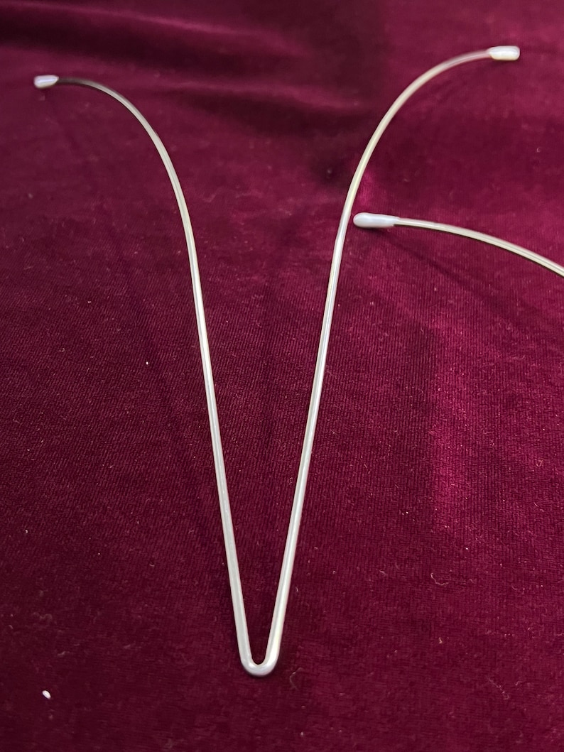 May include: Two silver wire hangers with white plastic tips. The hangers are bent into a V-shape.