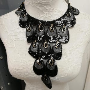 May include: A black beaded necklace with a cascading design. The necklace features teardrop-shaped embellishments with silver sequins and gold accents. The necklace is displayed on a white mannequin.