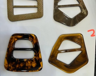 Puede incluir: Cuatro hebillas decorativas para cinturón de varias formas y colores. Las hebillas están numeradas del 1 al 4. Los colores incluyen marrón, carey y un beige texturizado. Las hebillas son de plástico o resina.