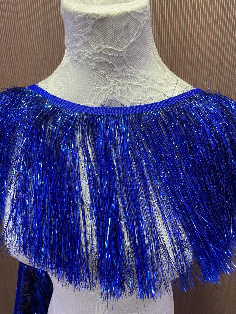 May include: A close-up of a blue fringe trim with a metallic sheen. The fringe is displayed on a white mannequin.