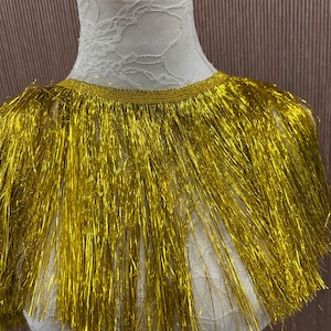 May include: Gold metallic fringe trim with a shiny finish. The fringe is approximately 1 inch in length.
