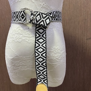 May include: A black and white woven belt with a silver ring buckle and a yellow leather tip. The belt is tied in a knot at the front.