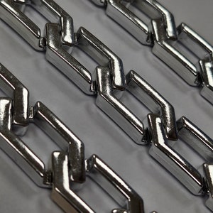 Könnte beinhalten: Nahaufnahme einer silbernen Kette mit einem Curb-Link-Muster. Die Kette ist aus Metall und hat eine glänzende Oberfläche.