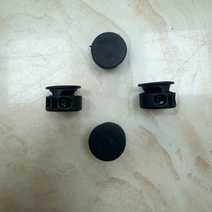 May include: Four black plastic toggle stoppers, two with a locking mechanism and two without.