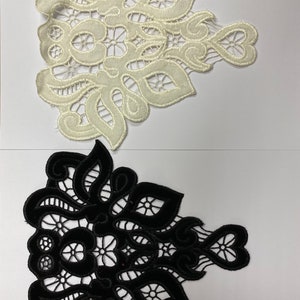 Puede incluir: Dos aplicaciones de encaje, una blanca y otra negra, con un delicado diseño floral. Las aplicaciones tienen forma de triángulo con bordes redondeados.
