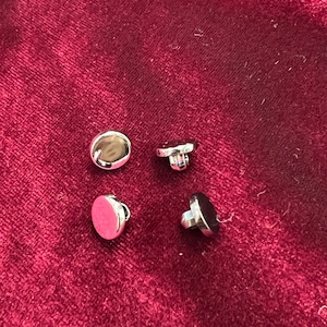 May include: Four silver-toned round buttons with a raised center. The buttons have a small hole in the center for sewing.