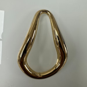 Puede incluir: Un anillo abstracto en forma de pera de color dorado con un acabado liso y pulido.