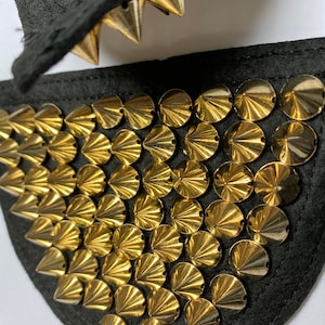 May include: A black fabric patch with gold-coloured, pointed, round studs. The studs are arranged in a pattern of rows and columns.