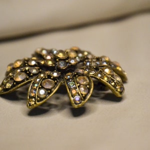 Puede incluir: Un broche de tono dorado con un dise&ntilde;o de flor, con diamantes de imitaci&oacute;n iridiscentes.