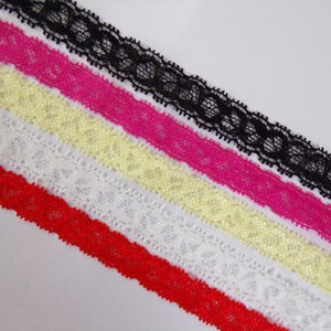 May include: Close-up of six strips of lace in various colours: red, white, yellow, pink, and black. The lace has a delicate, scalloped edge and a repeating floral pattern. The lace is likely used for sewing or crafting.