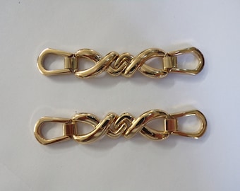 May include: Two gold-toned metal clasps with an intricate interwoven design. Each clasp has a loop on either end.