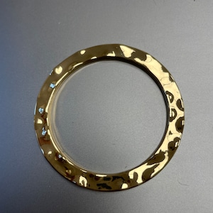 May include: A gold-toned hammered metal bangle bracelet. The bracelet is round and has a smooth, polished finish.