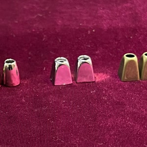 May include: Six metal cord end caps in three colours: silver, pink, and gold. The caps are shaped like small bells.