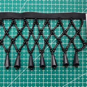 May include: Black beaded fringe trim with a diamond pattern and pointed tassels. The trim is measured against a ruler, showing it is approximately 9 cm long.