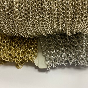 May include: Two spools of chain, one gold and one silver. The chains are both the same style, with a linked pattern.
