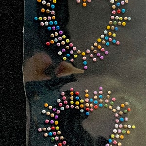 May include: Two heart-shaped designs made of colourful rhinestones on a black background. The rhinestones are arranged in a pattern that resembles a heart.