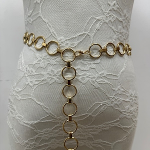 May include: A gold chain belt with large, round links. The belt is shown on a white lace mannequin.