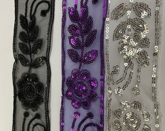Puede incluir: Tres tiras de adorno de lentejuelas negras, moradas y plateadas con diseños florales sobre un fondo de malla transparente.