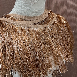 May include: Gold metallic fringe trim with a brown backing. The fringe is approximately 2 inches long.