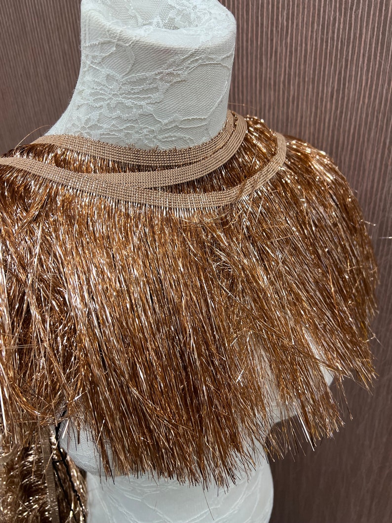 May include: Gold metallic fringe trim with a brown backing. The fringe is approximately 2 inches long.