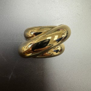 Puede incluir: Un anillo de color dorado con un diseño retorcido. El anillo está hecho de metal liso y brillante.