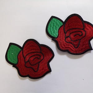 May include: Two red embroidered rose patches with green leaves. The roses have a black outline.