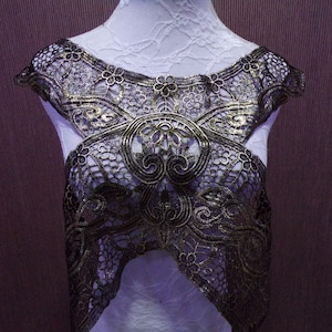 May include: A gold-colored lace trim with a delicate floral pattern. The lace is on a white background and has a scalloped edge.