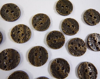 May include: A collection of 14 round, bronze-coloured buttons with a textured surface and two holes. The buttons have a distressed look.