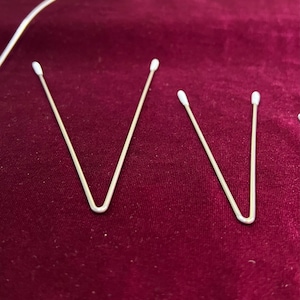 May include: Three silver metal V-shaped hair clips on a burgundy fabric background.
