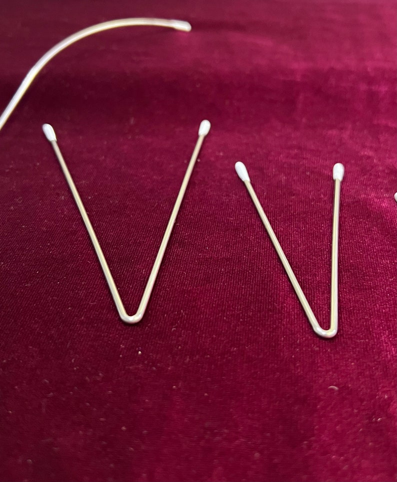 May include: Three silver metal V-shaped hair clips on a burgundy fabric background.