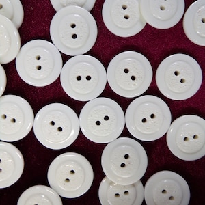 May include: A collection of white plastic buttons with two holes each. The buttons are arranged in a circular pattern on a red background.