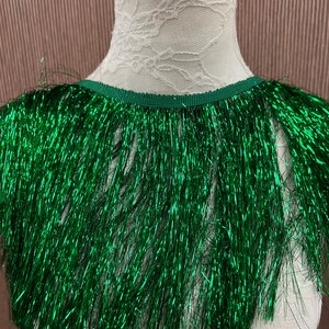 May include: Green metallic fringe trim with a shiny finish. The fringe is approximately 1 inch long and is attached to a narrow green ribbon.