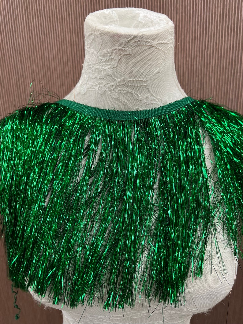 May include: Green metallic fringe trim with a shiny finish. The fringe is approximately 1 inch long and is attached to a narrow green ribbon.