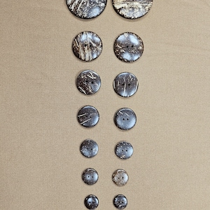 May include: A set of 12 brown coconut shell buttons with two holes each. The buttons are arranged in two columns, with the largest buttons at the top and the smallest buttons at the bottom.