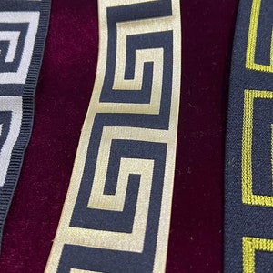 Puede incluir: Primer plano de tres cintas decorativas con patrones geom&eacute;tricos. Las cintas presentan dise&ntilde;os en negro y dorado, negro y amarillo y negro y blanco. Las cintas se muestran sobre un fondo de terciopelo rojo oscuro.