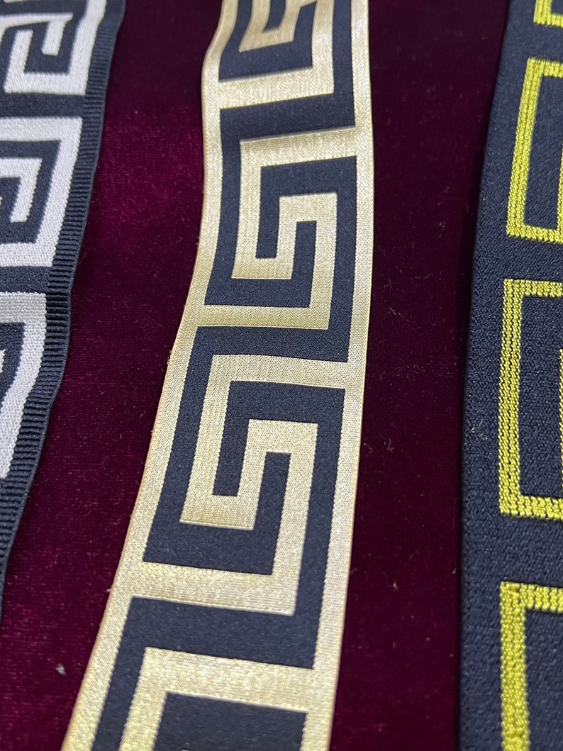 Puede incluir: Primer plano de tres cintas decorativas con patrones geom&eacute;tricos. Las cintas presentan dise&ntilde;os en negro y dorado, negro y amarillo y negro y blanco. Las cintas se muestran sobre un fondo de terciopelo rojo oscuro.