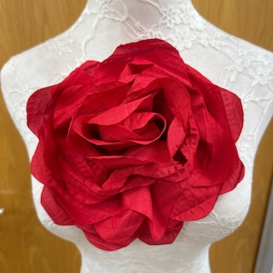 Peut inclure: Une grande rose en tissu rouge. La rose est sur un mannequin recouvert de dentelle blanche.