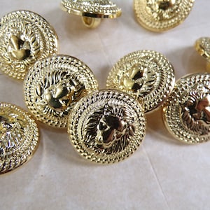 Puede incluir: Un grupo de ocho botones de metal dorado con un dise&ntilde;o de cabeza de le&oacute;n. Los botones tienen un dise&ntilde;o en relieve texturizado y un acabado brillante.