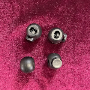 May include: Four black plastic toggle clasps with a spring mechanism. The clasps are round and have a small hole on the side.