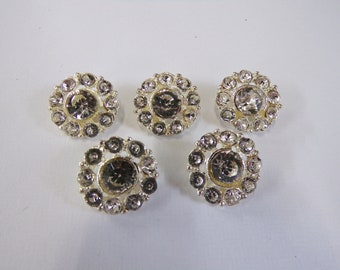 May include: Five silver-toned round buttons with clear rhinestones arranged in a circle around a larger clear rhinestone in the center.