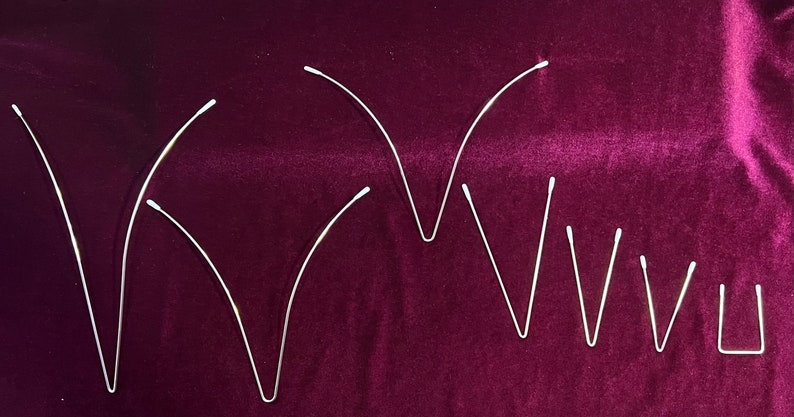 May include: A set of nine silver-colored metal hair clips in various sizes and shapes. The clips are arranged in a row on a burgundy velvet surface.