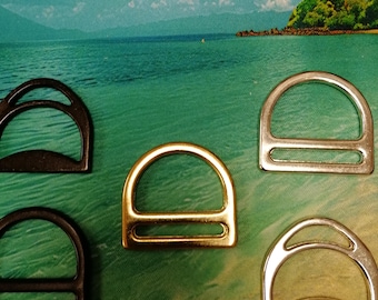 May include: An assortment of D-rings in various metallic finishes, including gold, silver, and black. The hardware is arranged against a backdrop of a tropical beach scene, showcasing the rings' shapes and colors.