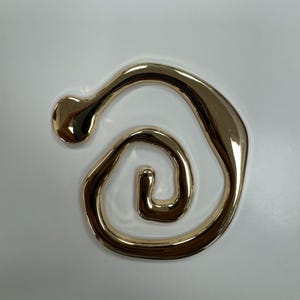 May include: A gold-colored abstract swirl design earring. The earring is made of a smooth, shiny metal and has a unique, organic shape.