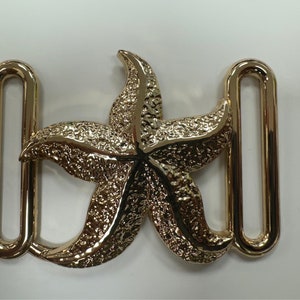 Pode incluir: Fivela de cinto dourada com um design de estrela do mar detalhado.